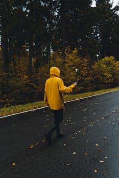 A person wearing a yellow hoodie walking on a forest road in autumn while holding a torch.