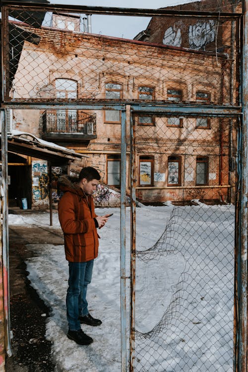 A Man in Brown Jacket and Denim Jeans Standing on a Snow Covered Ground