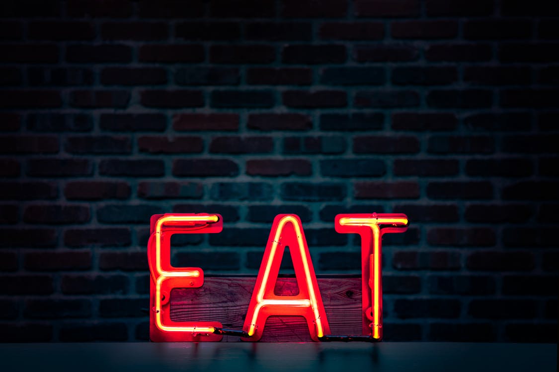 An image of a red neon sign which reads "EAT" on a brick background. 