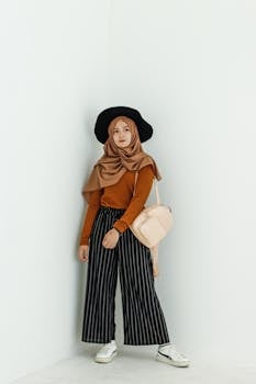 一位戴着时尚头巾的女士倚靠在极简主义的白墙上，展现出时尚的造型