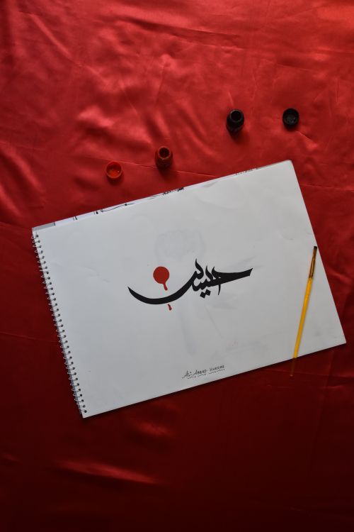 Free Artistic Arabic calligraphy on sketchbook with paintbrush and inks on red background. Stock Photo