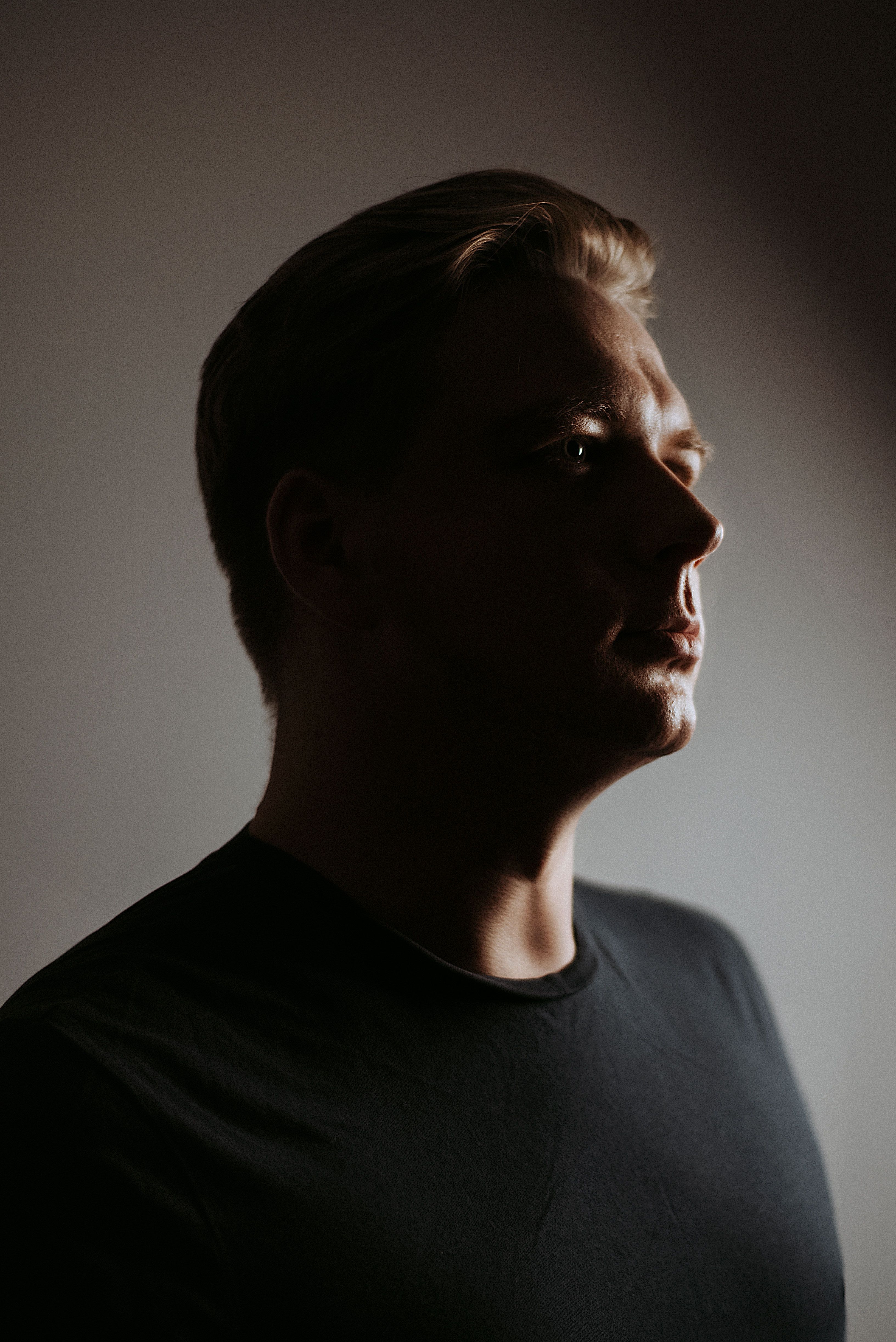 Dramatic half-profile portrait of a man, face split by light and shadow, gazing away from the camera
