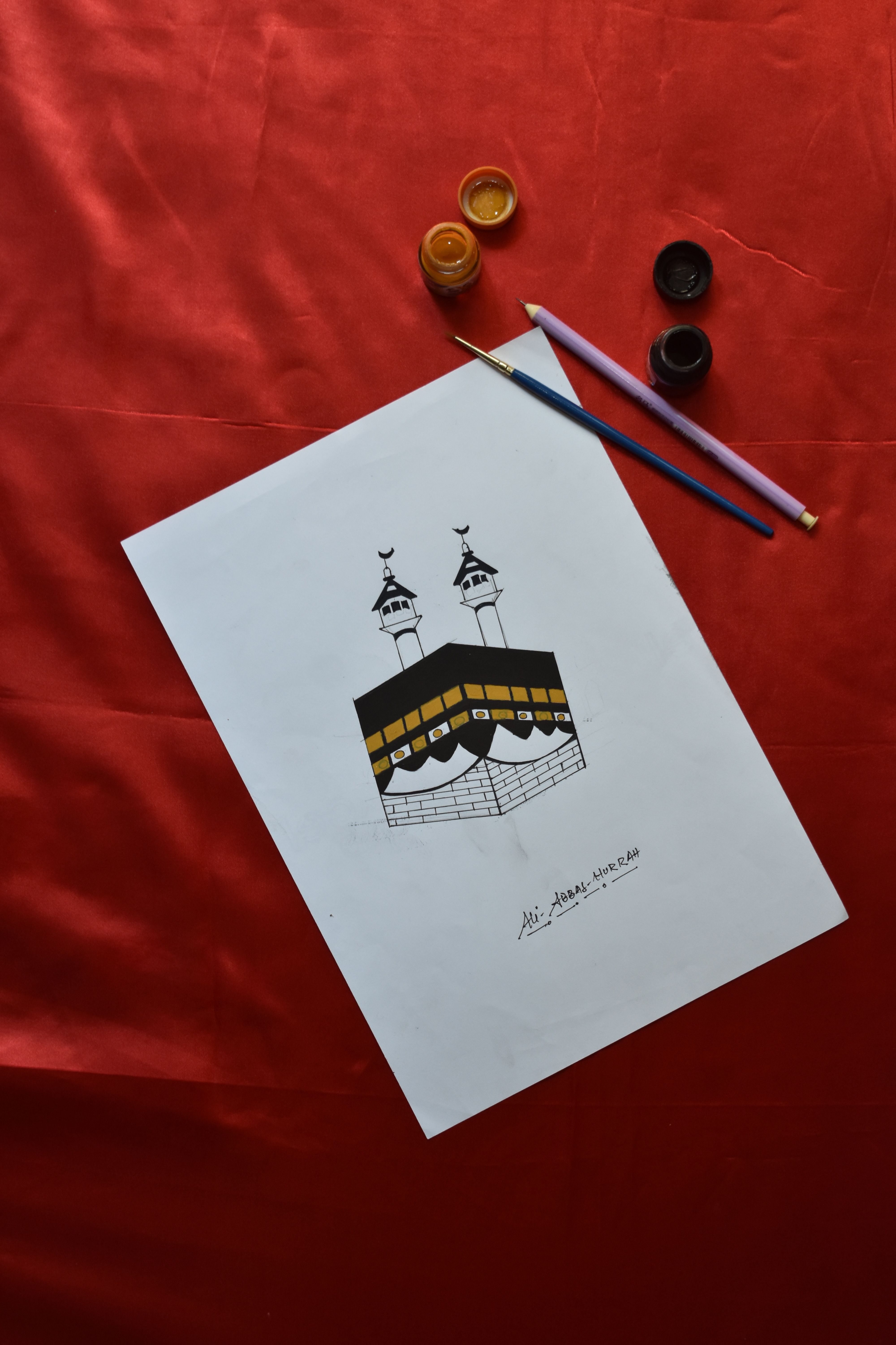 A detailed pencil drawing of the Kaaba with painting tools on a red background.