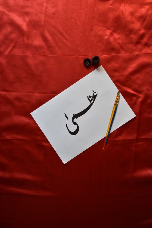 Free Artistic Arabic calligraphy on paper with pen, creating a decorative still life on a red surface. Stock Photo