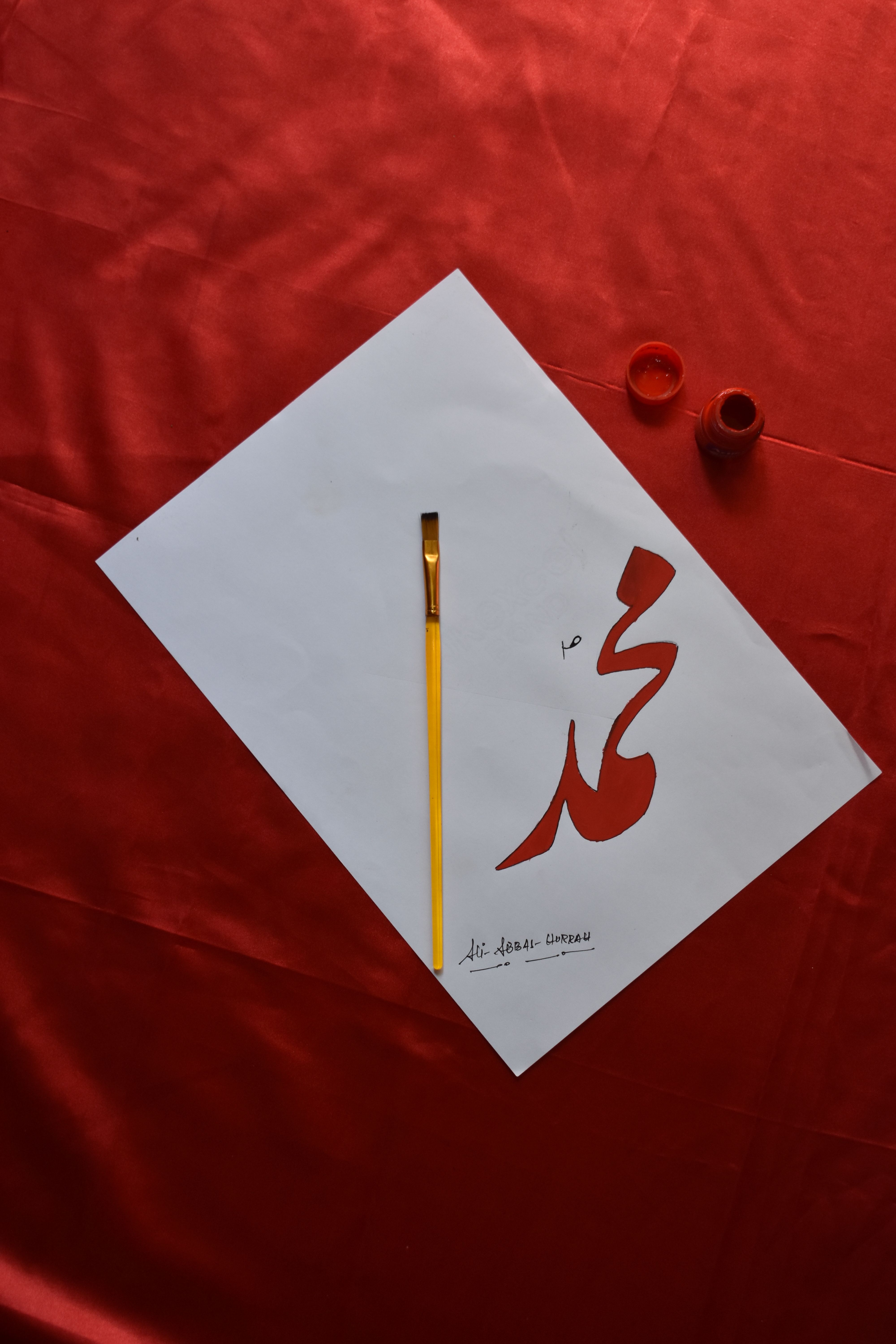 Top view of artistic calligraphy beside a paintbrush on a vibrant red background.