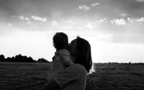Free Heartwarming silhouette of a mother kissing her baby in an open field, capturing a tender moment. Stock Photo