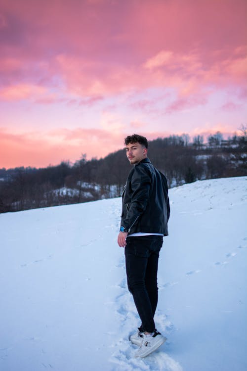 A Man in Black Leather Jacket and Black Pants Standing on a Snow Covered Ground