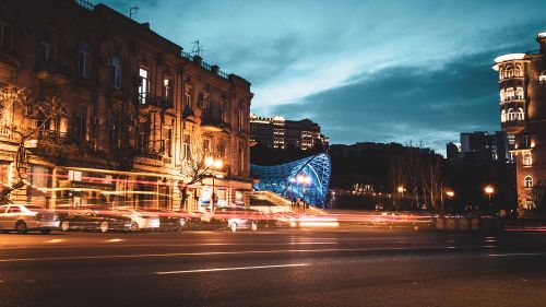 Free Dynamic night scene of a city with light trails and a glowing modern bridge, creating a vibrant urban atmosphere. Stock Photo