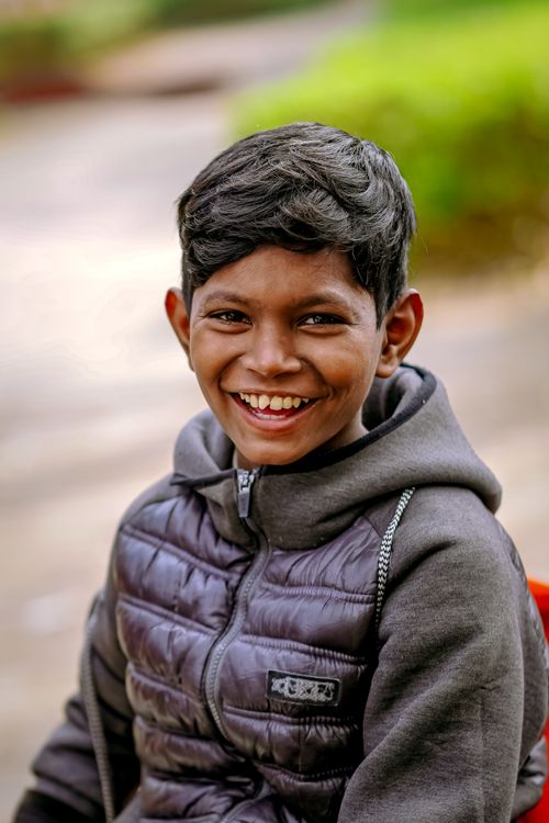 Free A joyful boy in a warm jacket sitting outside, smiling happily. Stock Photo
