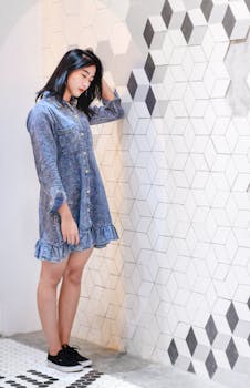 一位年轻女子身着时尚牛仔连衣裙，在室内几何图案墙壁旁摆姿势的肖像