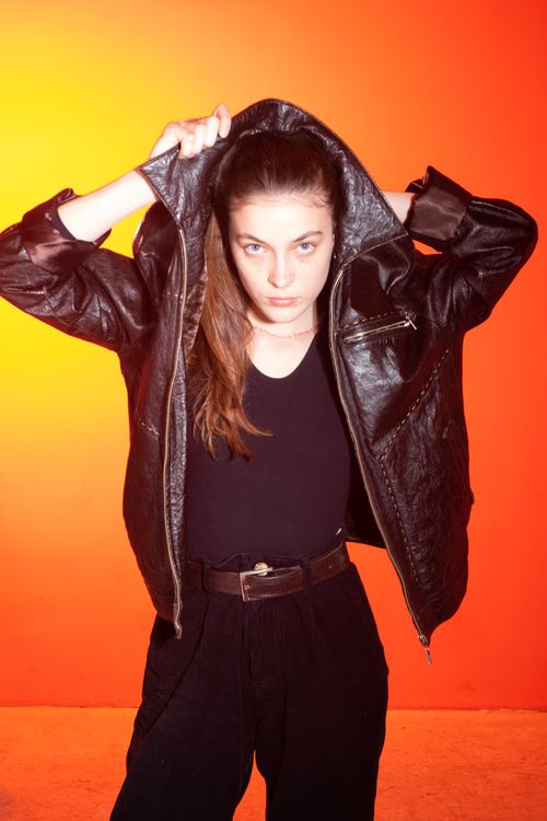 Free Stylish woman in a black leather jacket against a vibrant orange background, exuding confidence and elegance. Stock Photo