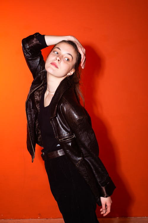 Free Fashion portrait of a woman in a black leather jacket posing against a vibrant red background. Stock Photo
