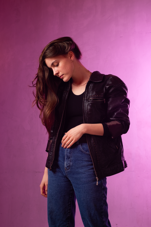 Free Stylish woman in black leather jacket and jeans against a purple background. Stock Photo