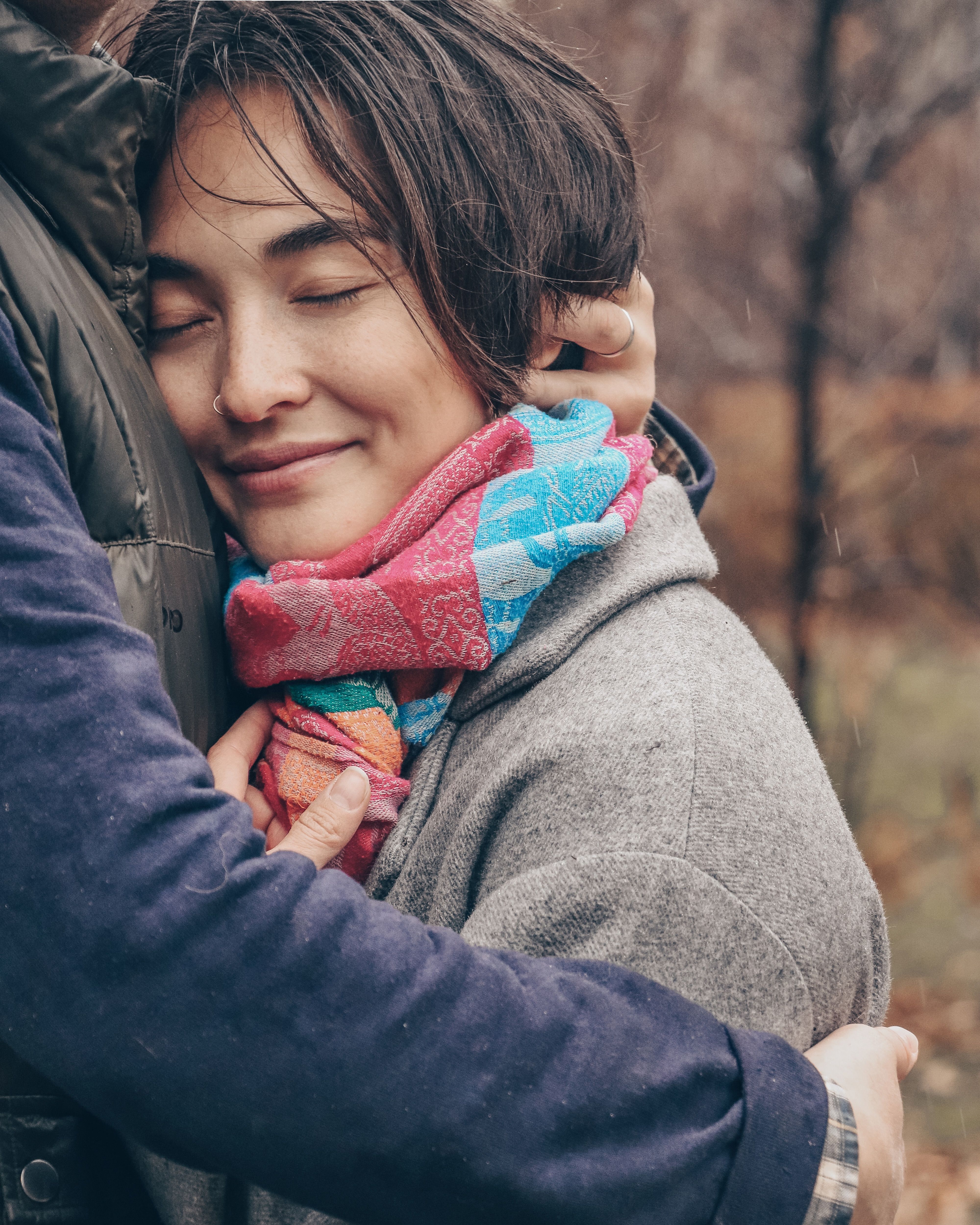 Close-up portrait of a smiling woman embraced warmly outdoors with a colorful scarf.