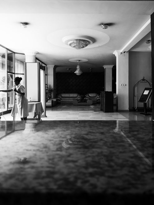 Free Black and white photo of a housekeeper cleaning a luxury hotel interior, emphasizing elegance and cleanliness. Stock Photo