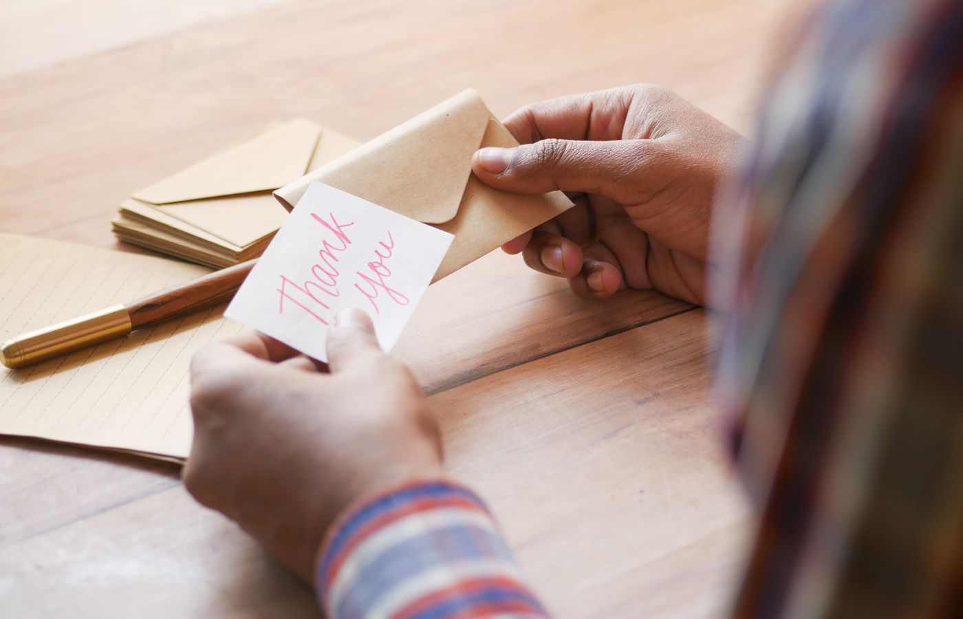 Close-up of hands holding a thank you note in an envelope on a table.