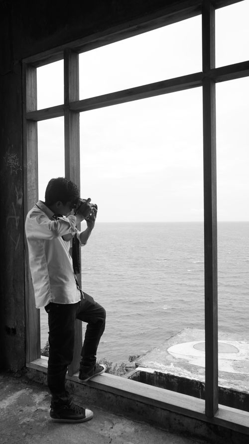 Free Young man taking photos of sea view from a window in West Nusa Tenggara, Indonesia. Stock Photo
