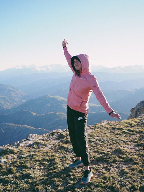 Woman in Pink Hoodie Jacket Raising Her Hand on Mountain Top