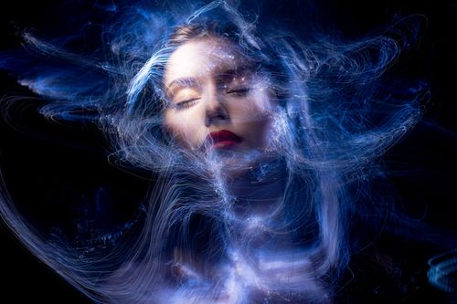 Free Abstract portrait of a woman with swirling blue light trails and closed eyes. Stock Photo