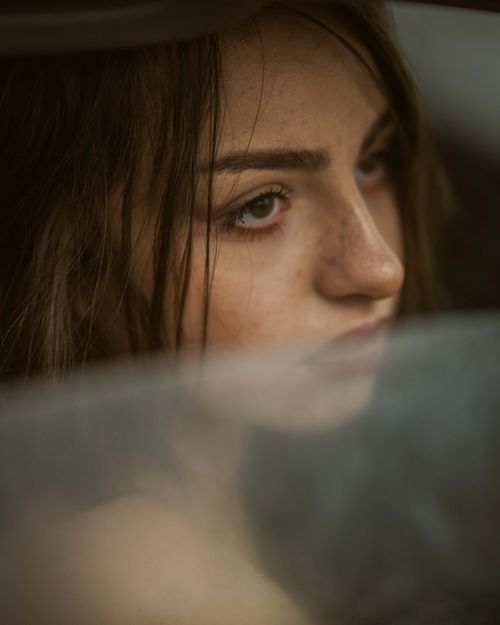Free Close-up portrait of a contemplative young woman gazing through a blurred window, capturing a moody expression. Stock Photo
