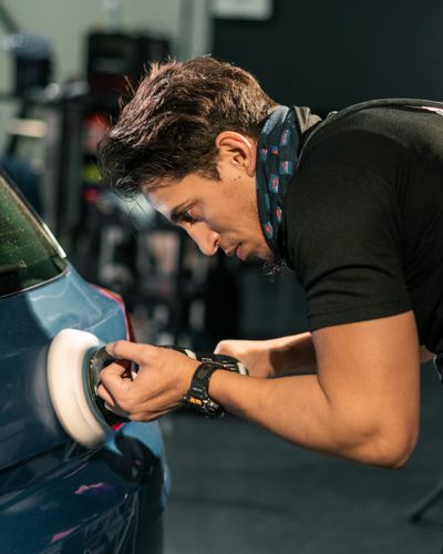 Technician polishing car paint with a buffing machine indoors