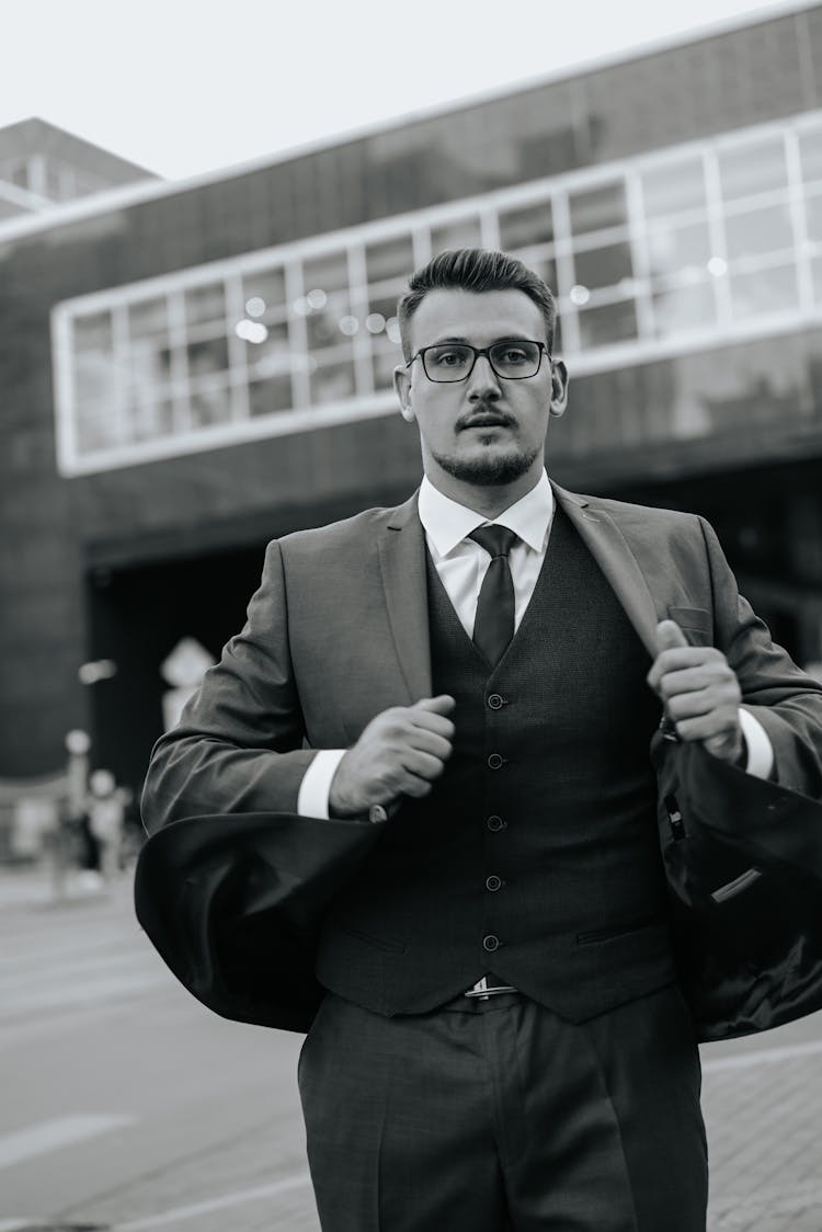 Black And White Portrait Of Man In Glasses Walking And Fixing His Suit