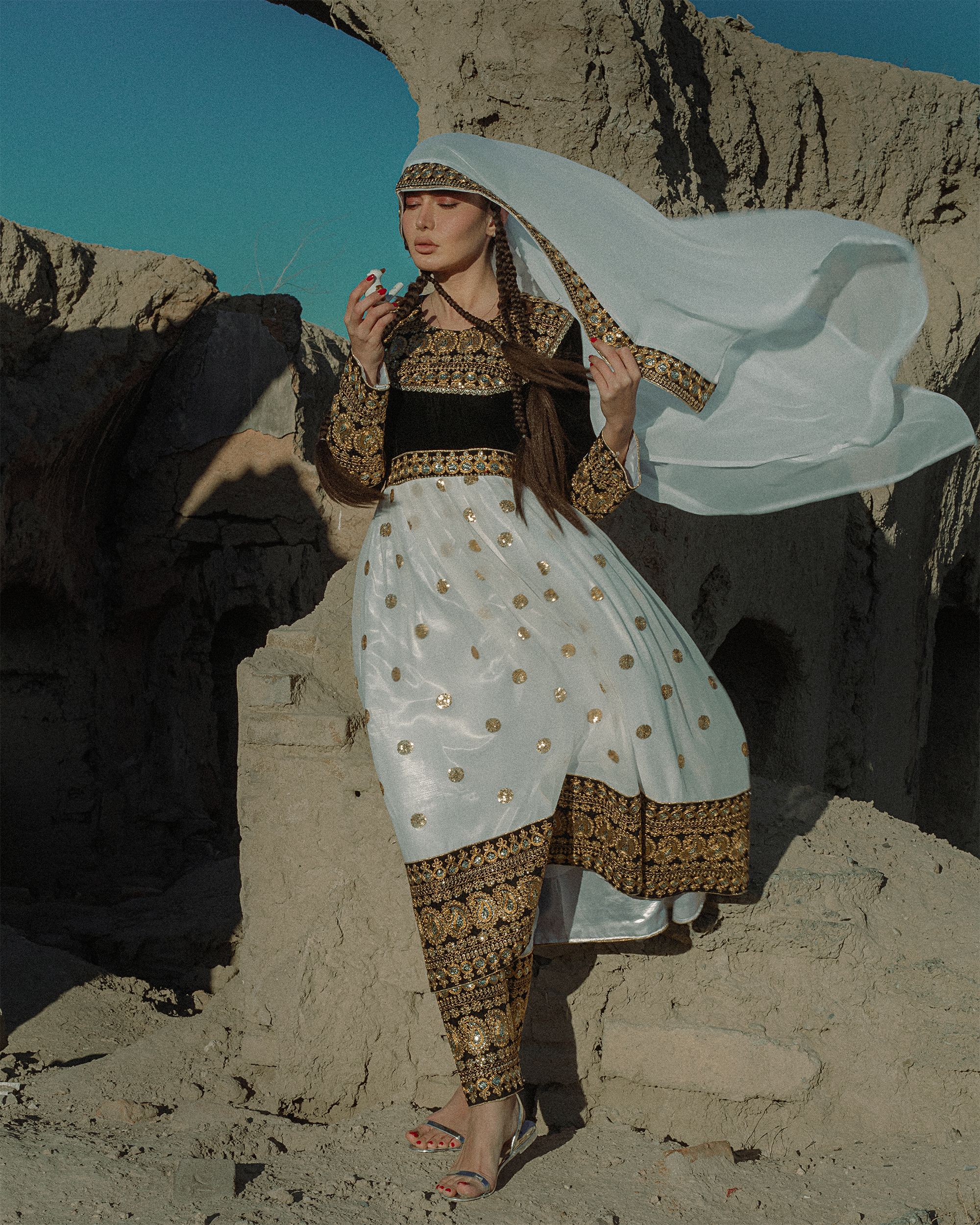 Stylish woman posing in traditional dress amidst a desert landscape, embracing cultural elegance.
