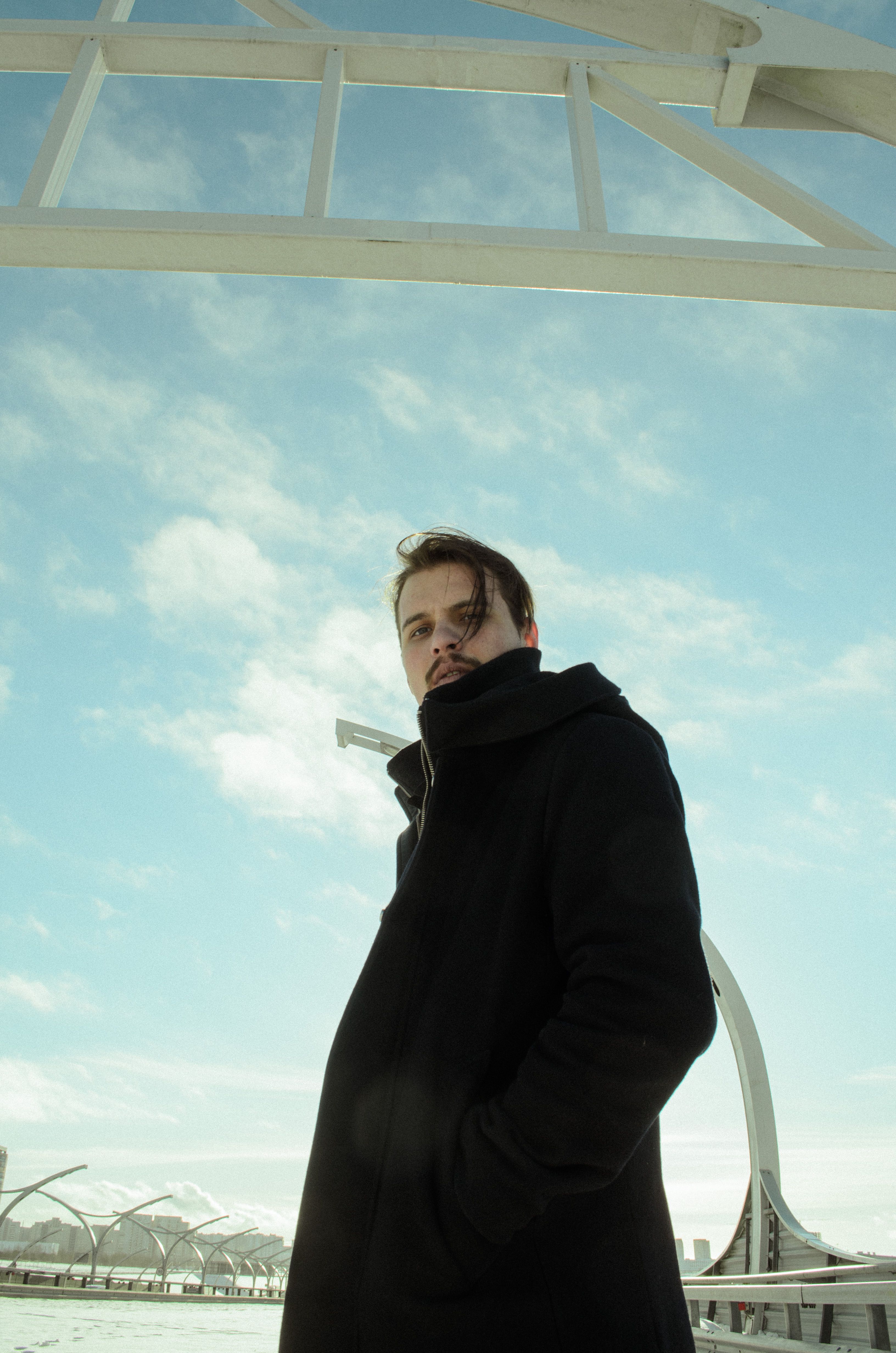 Low-angle shot of a man in a black coat against a blue sky outdoors.