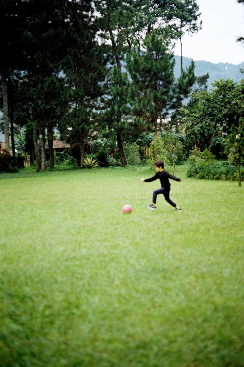 A Young Boy in Black Long Sleeves Playing on Green Grass Field