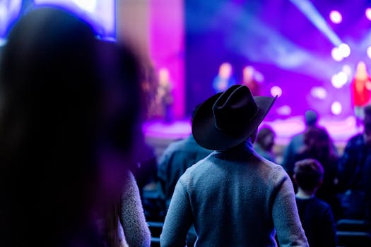 Back view of an audience with a cowboy hat at a night concert with vibrant lights.