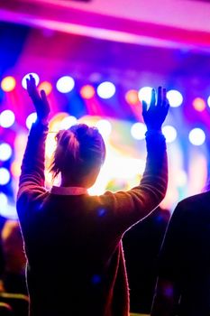 Excited concertgoer raising hands amidst vibrant stage lights.