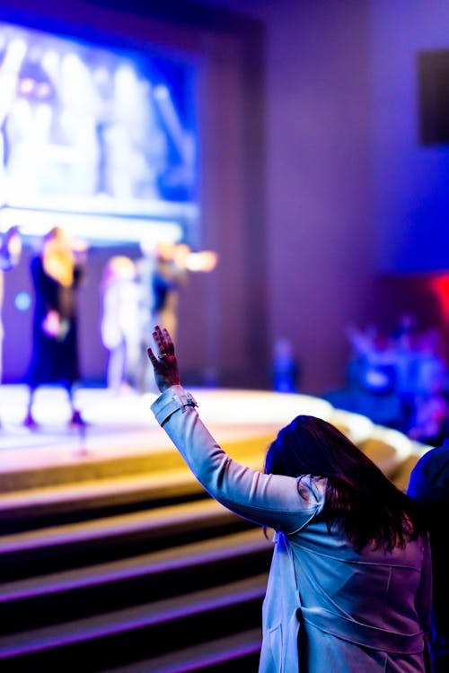 Woman Raising Hand in Front of the Stage During a Concert