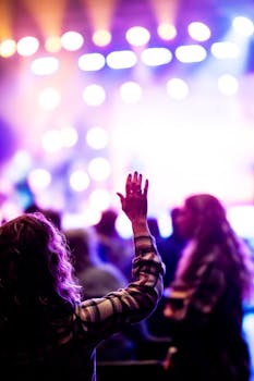 Colorful concert scene with vibrant lights and crowd enjoying the music with hands raised.