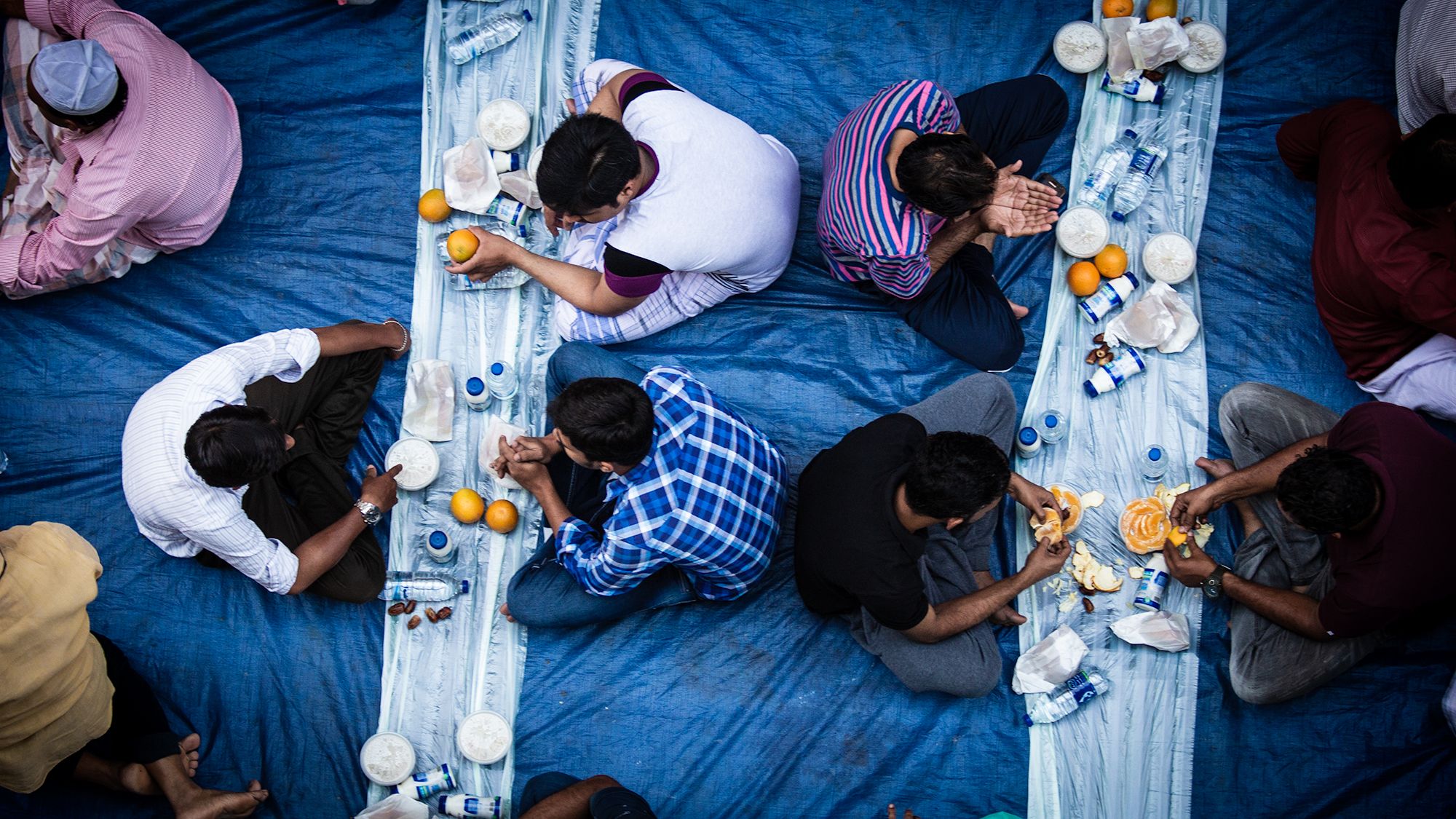 Top view of a group enjoying Iftar meal on blue fabric during Ramadan fasting period.