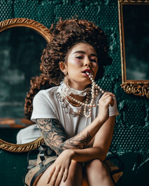 Free A creative portrait of a woman with a wig, pearl necklace, and tattoos, posing stylishly indoors. Stock Photo
