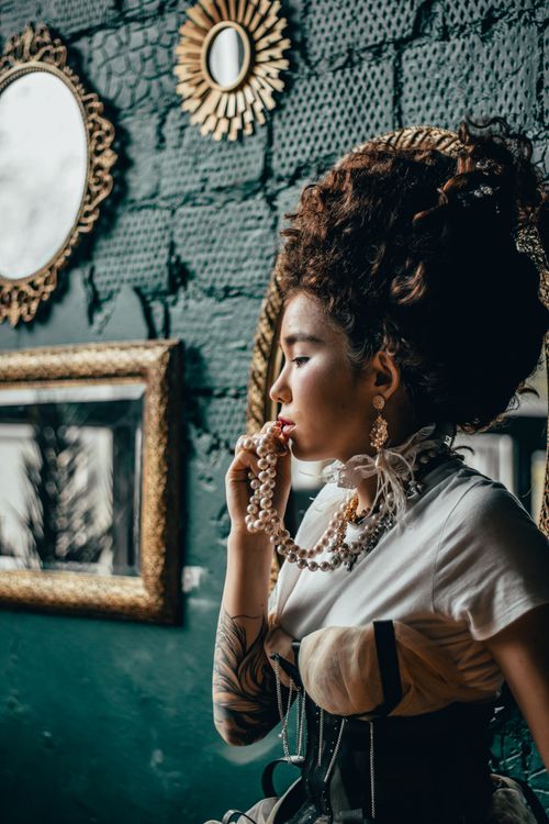 Free Stylish portrait of a woman holding a pearl necklace in a vintage-themed room. Stock Photo