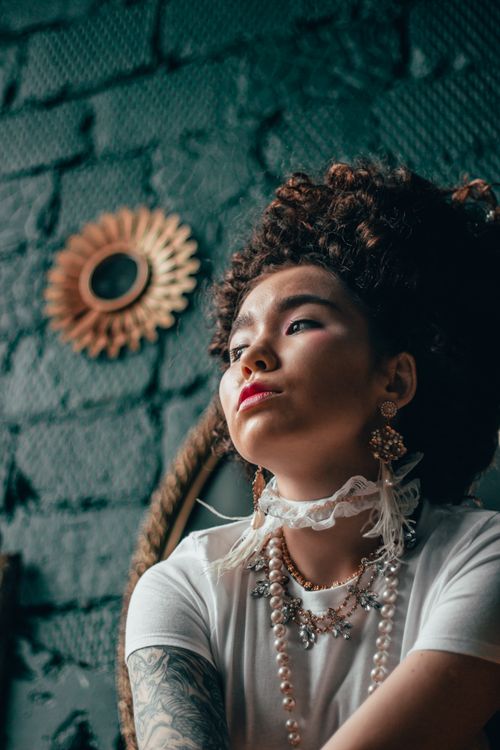 Free A striking portrait of a woman with intricate jewelry and unique hairstyle against a textured wall. Stock Photo