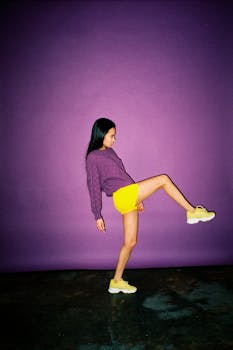Fashionable woman in vibrant attire striking a playful pose in a studio setting.