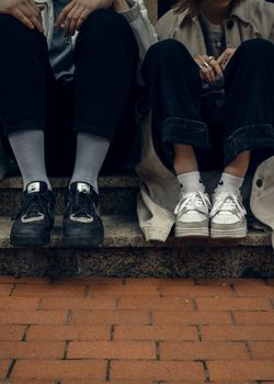Two young adults sitting on steps wearing casual sneakers and dark jeans.