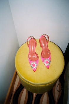 Stylish bright pink heels with jeweled accents on a yellow ottoman.