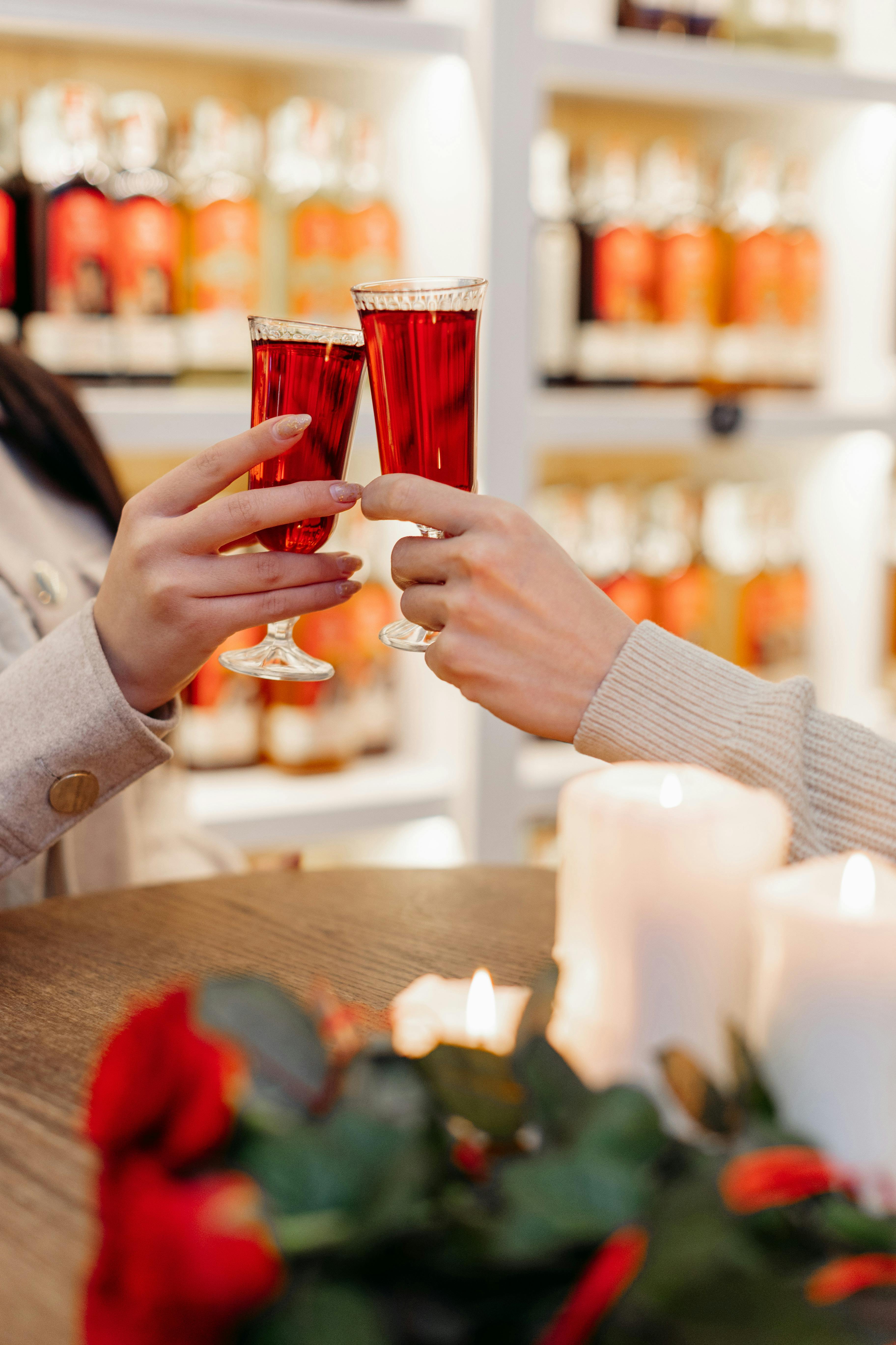 Two hands holding glasses of red wine in a festive setting with roses.