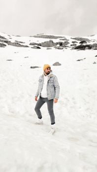 Man with beanie and jacket posing on a snowy winter landscape, showcasing winter fashion.