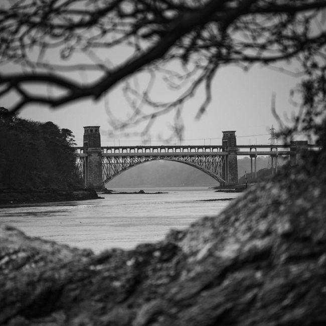 A dramatic monochrome image of Britannia Bridge spanning the Menai Strait in the UK.
