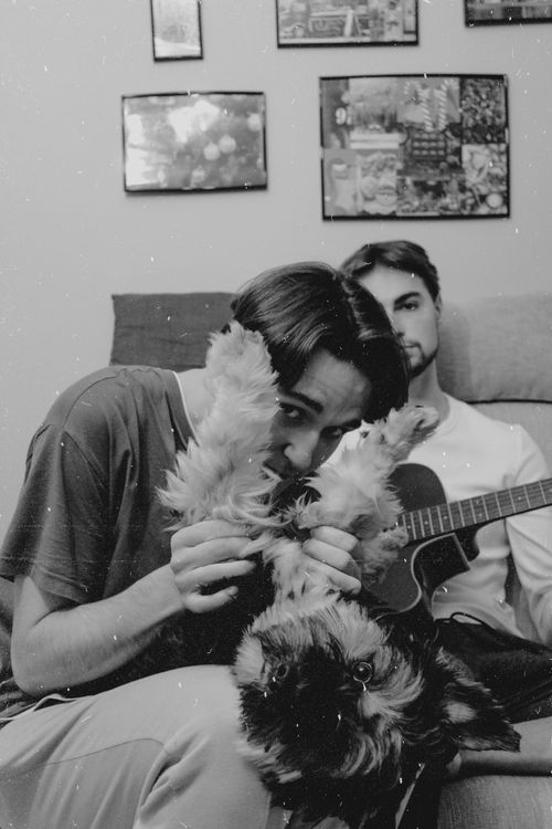 Free A candid black and white photo of two men relaxing with a dog and an acoustic guitar indoors. Stock Photo