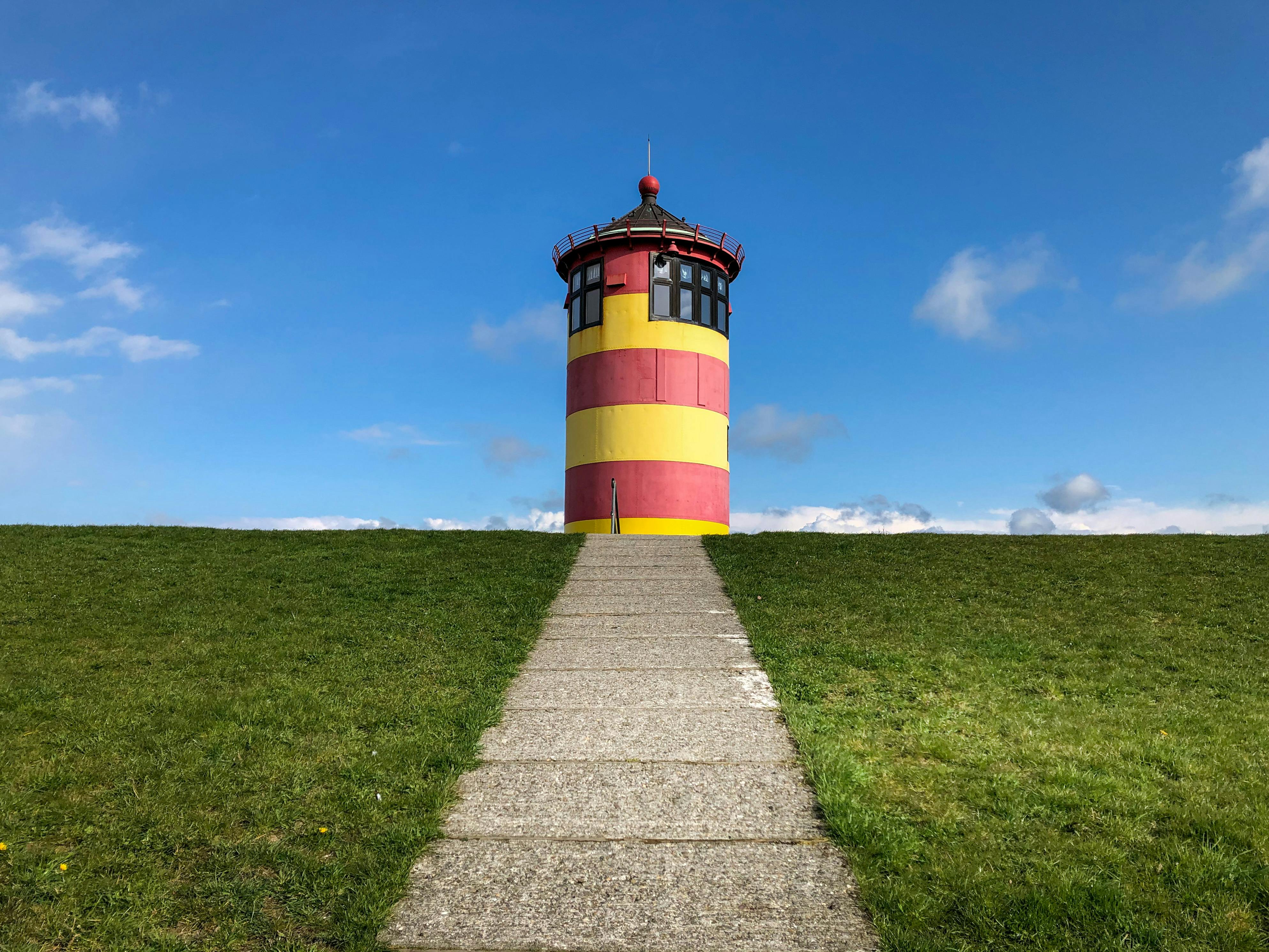 Red and Yellow Lighthouse on a Grassy Field · Free Stock Photo