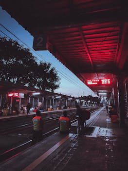 A quiet train station at dusk with passengers waiting under red lights, capturing a moody urban atmosphere.