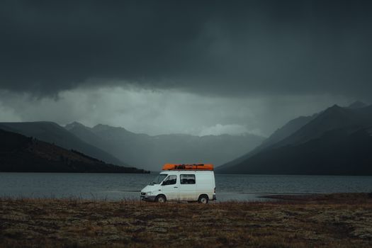 A lone van parked by a serene mountain lake under a dramatic, overcast sky, ideal for travel and adventure themes.
