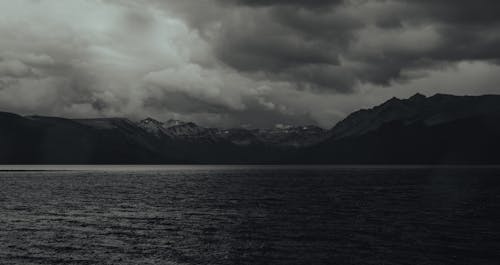 Grayscale Photo of Mountains in Front of a Sea