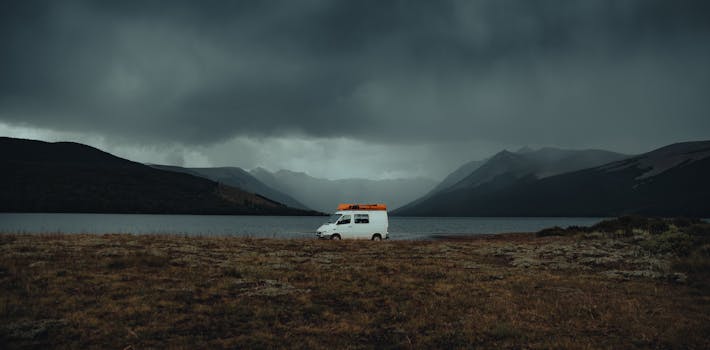 A lone van traverses a scenic route with mountains and fog, offering a sense of adventure.
