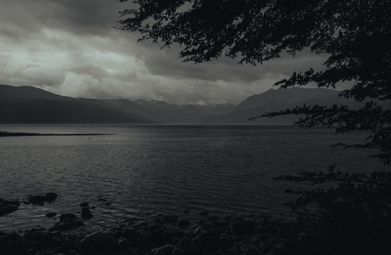serene monochrome lake with mountain backdrop and dramatic cloud cover